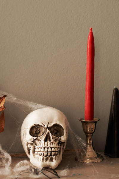 Skull with Cobweb Stands next to Red Halloween Candle